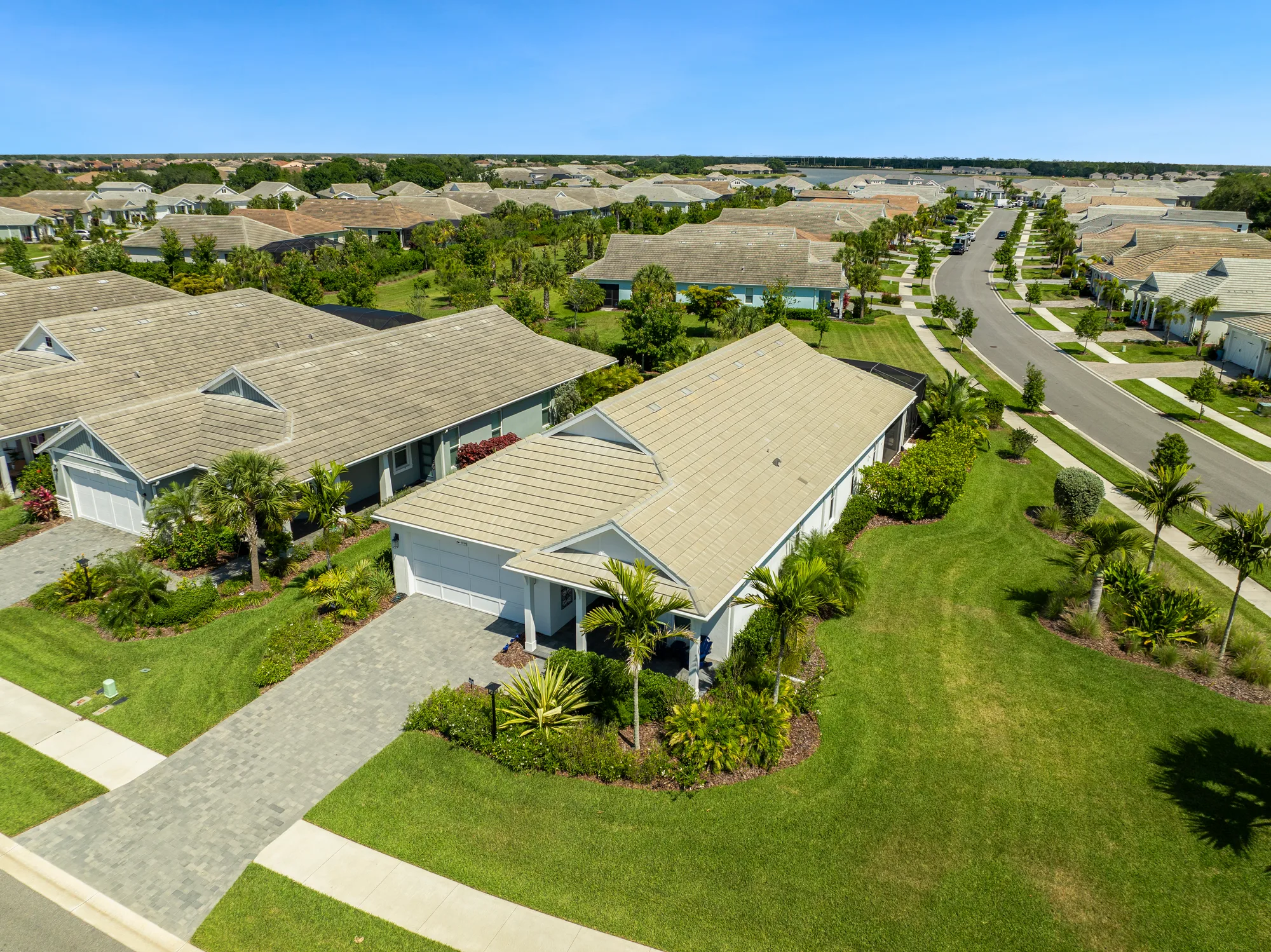 This image captures an aerial view of a peaceful suburban neighborhood featuring well-maintained houses, manicured lawns, and palm trees. The roads are lined with greenery, showcasing a serene community atmosphere.