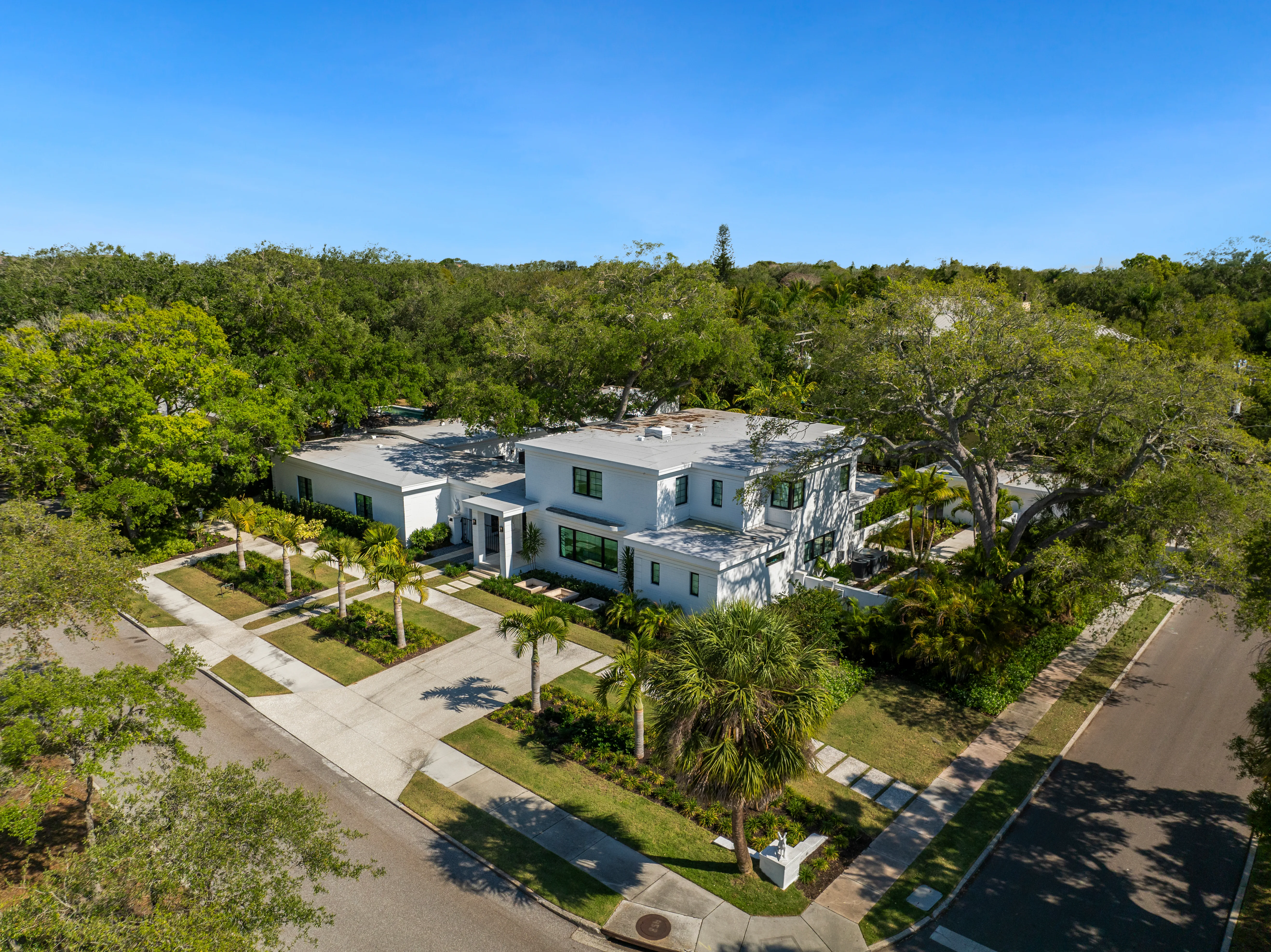 Aerial of a contemporary white house surrounded by lush landscaping and mature trees.
