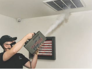 A technician using a fogging machine to treat air ducts in a room