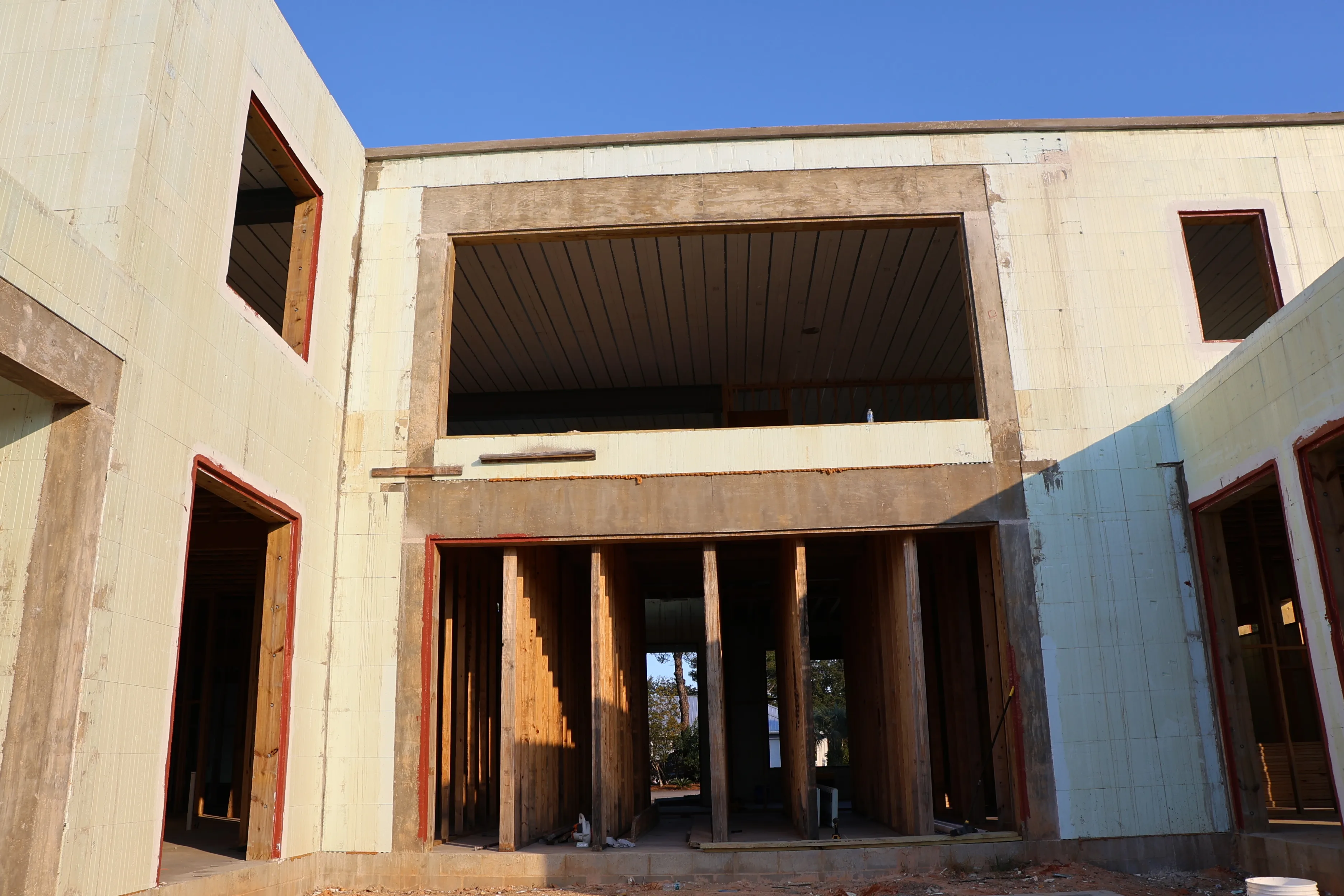 The front of a concrete house shell under construction with a wide braced opening at ground level.