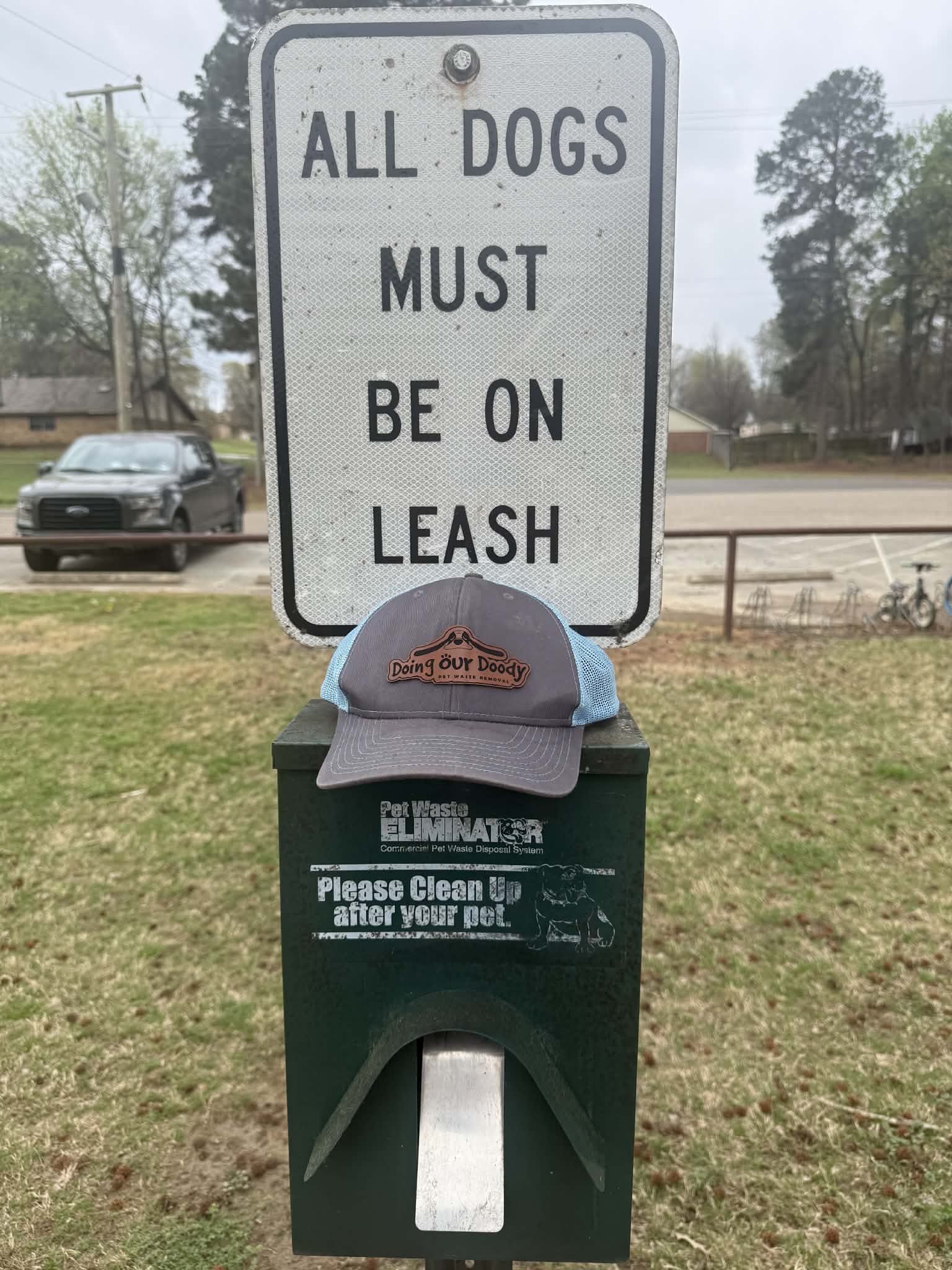 All Dogs Must Be On Leash sign mounted on a post next to a Pet Waste Eliminator disposal unit in a grassy area