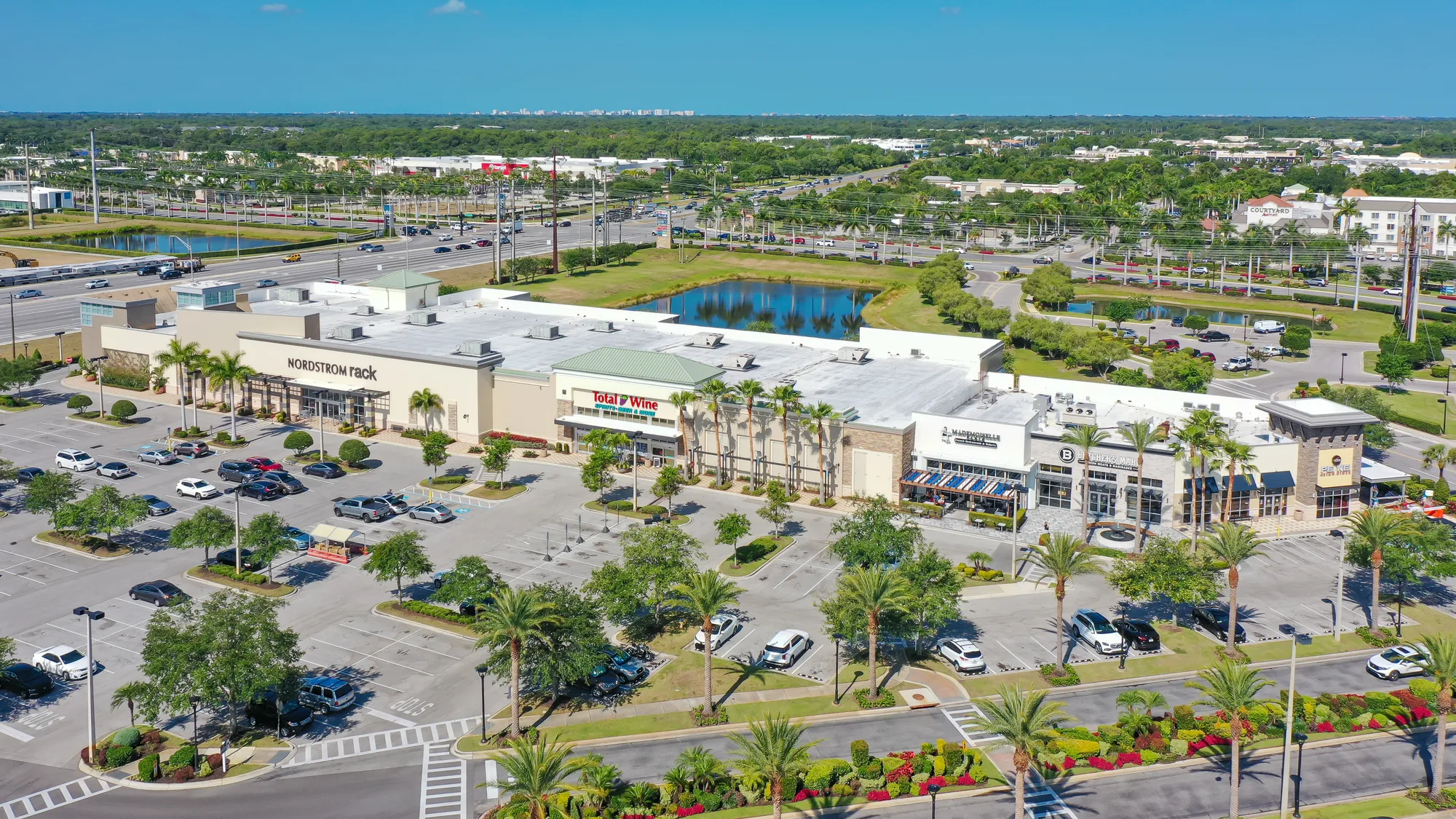 Aerial of the University Town Center retail buildings and landscaped parking, with palms lining the drives.