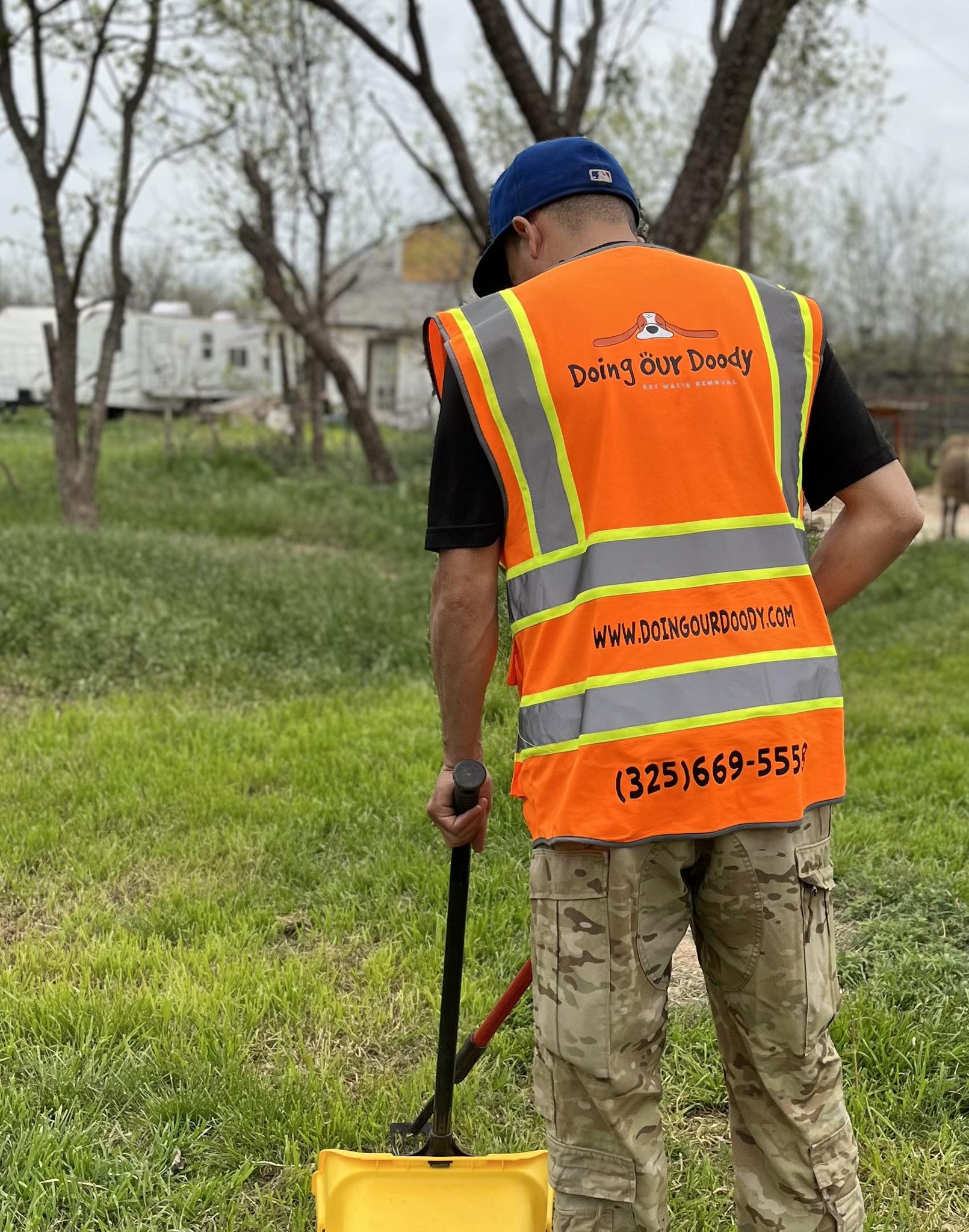 Doing Our Doody technician in branded orange vest holding a shovel in a residential yard