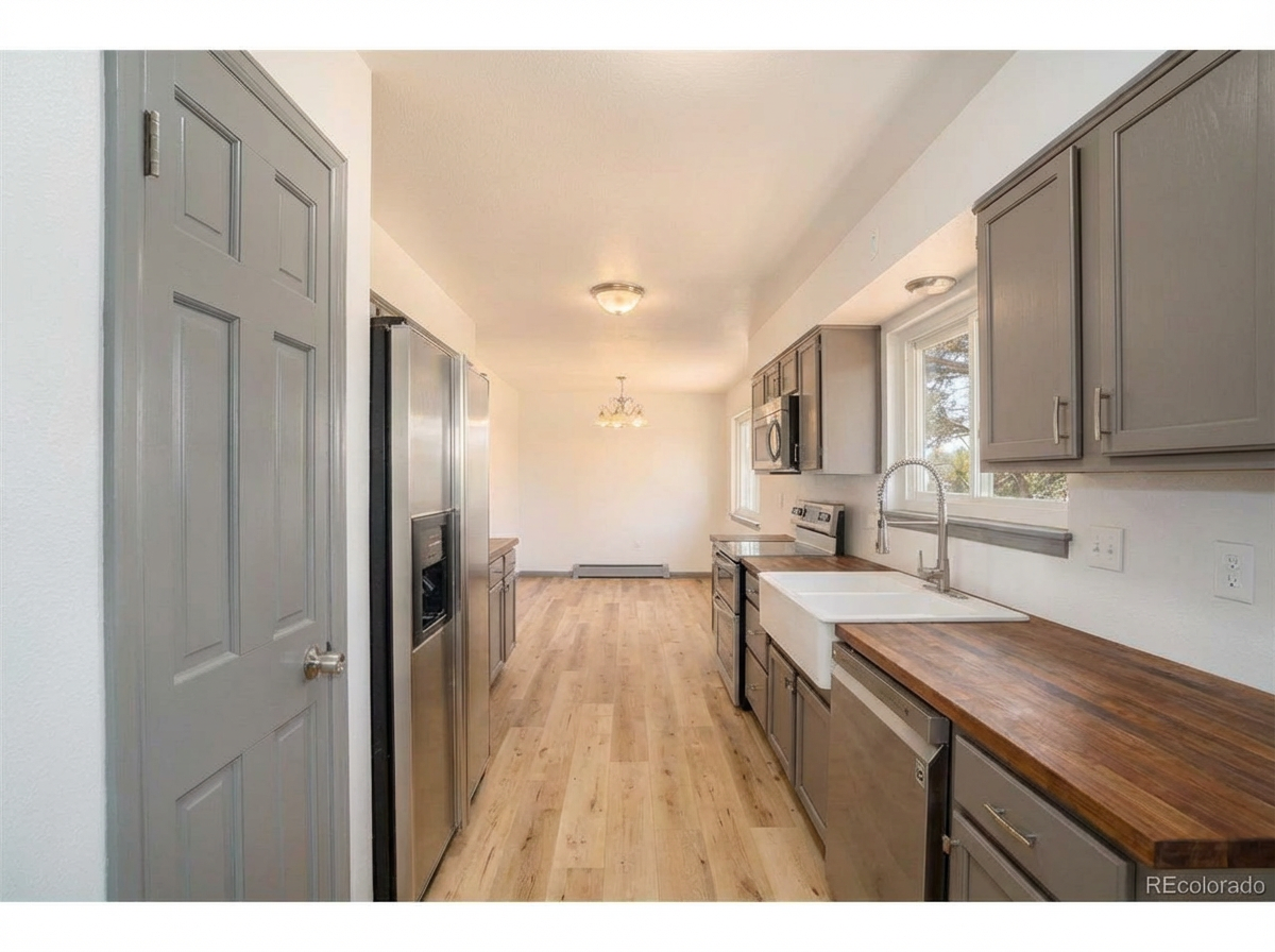 Modern kitchen with stainless steel appliances, gray cabinetry, wooden countertop, and chandelier