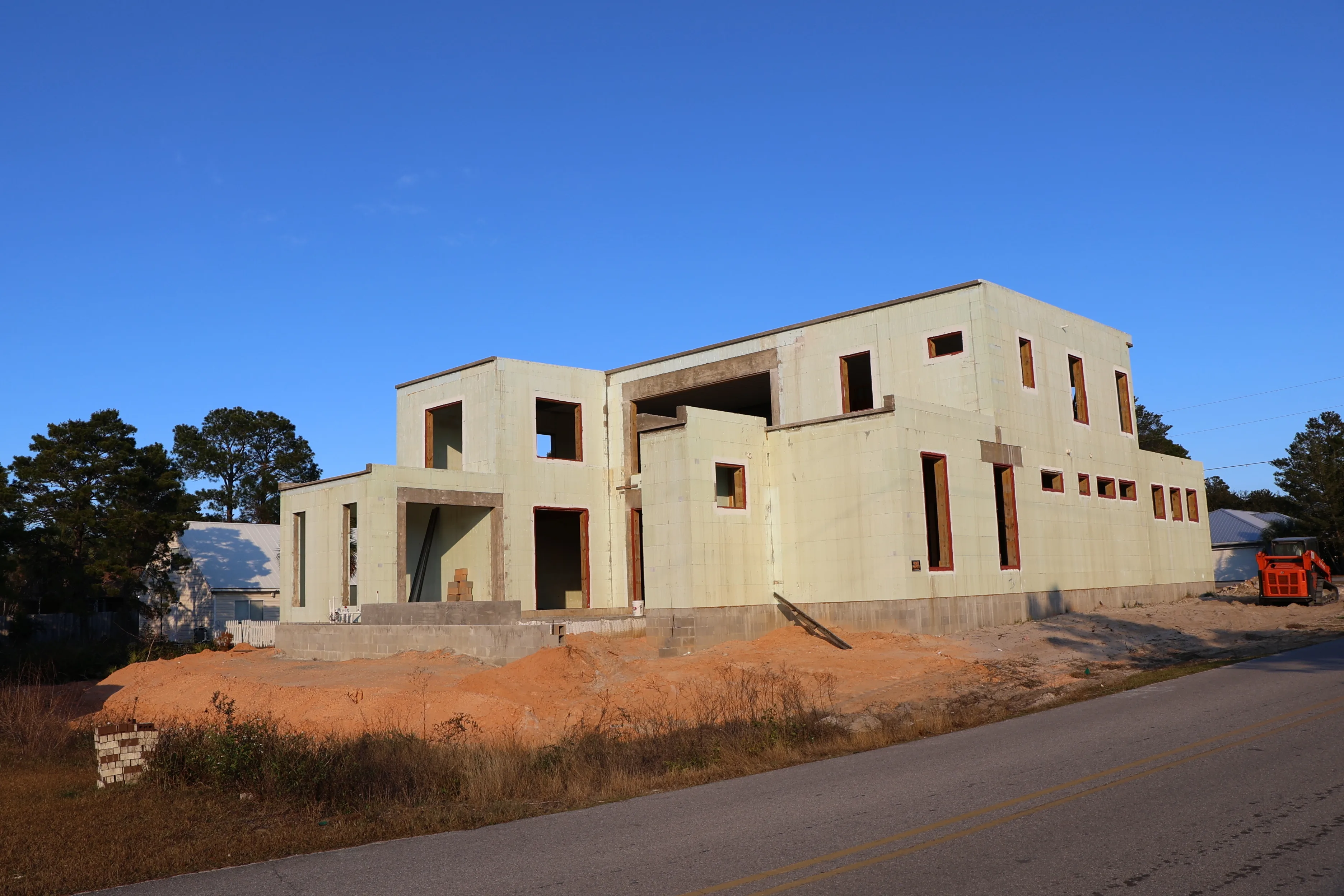 A partially constructed house on a raised sandy lot under a clear blue sky.