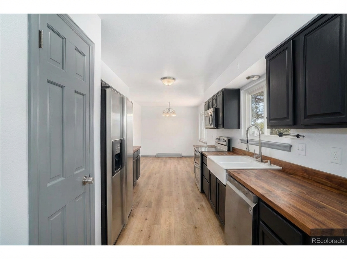 Spacious modern kitchen with dark cabinets, stainless steel appliances, wooden countertop, and farmhouse sink
