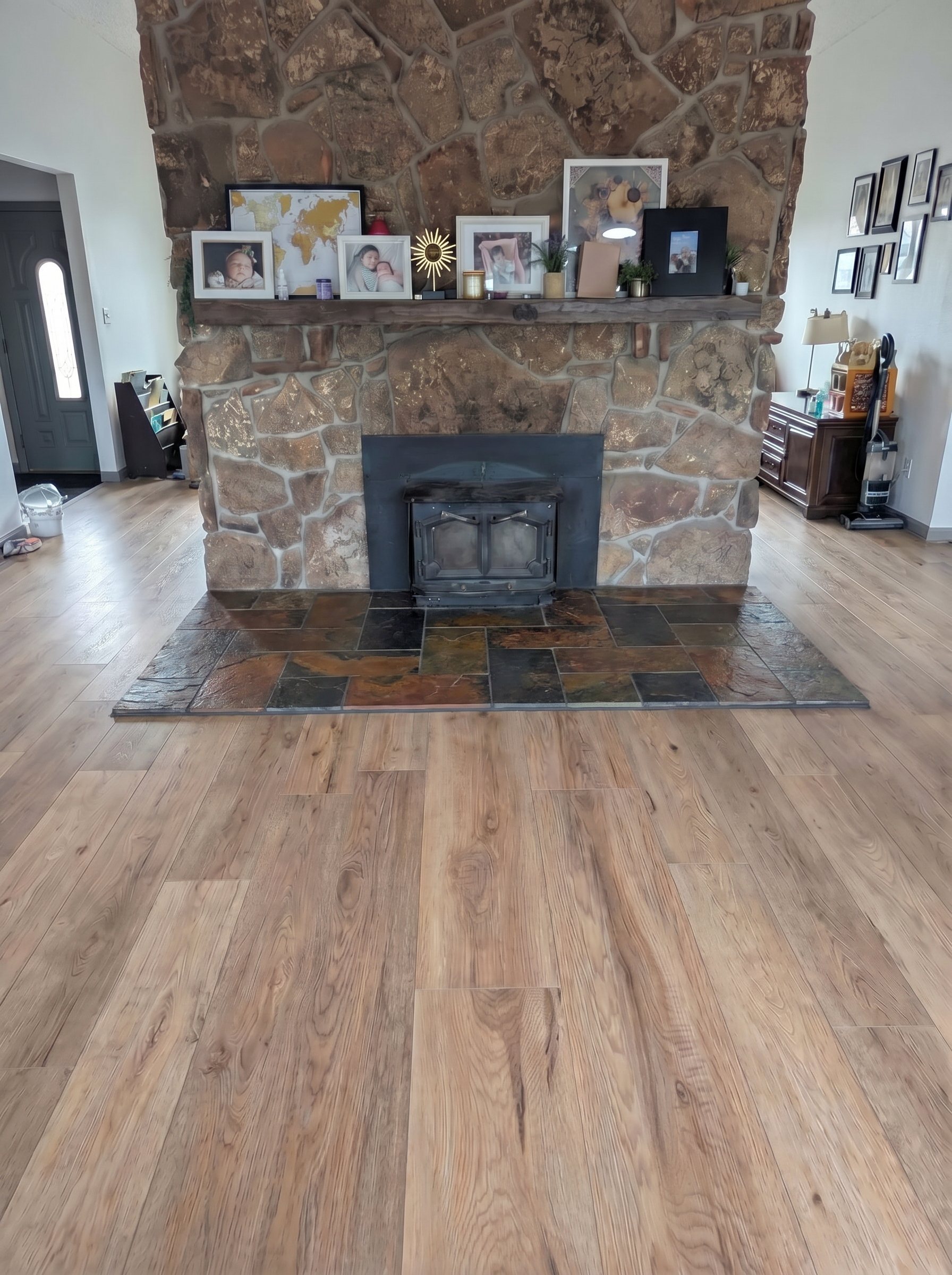 Spacious living room with a stone fireplace featuring a black insert and family photos on the mantel