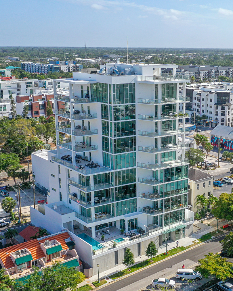 Aerial of the white multi-storey Peninsula Residences building with its pool deck, the Sarasota marina behind it.