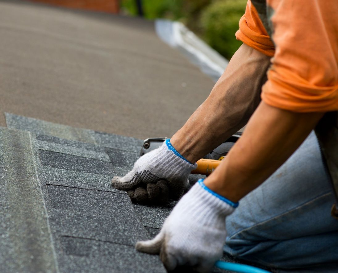 Close-up of a roofer's gloved hands installing asphalt shingles on a Treasure Coast home