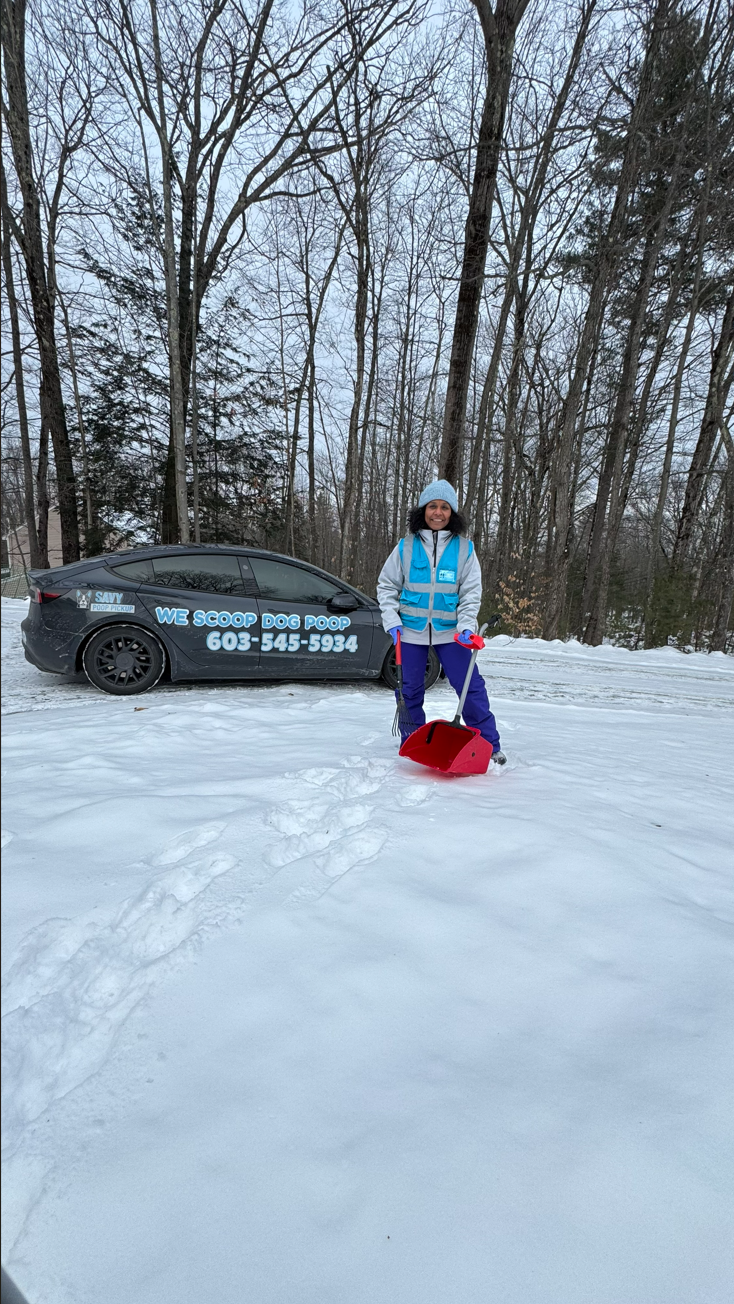 Technician in winter gear holding a red shovel beside the Savy Poop Pickup vehicle in the snow