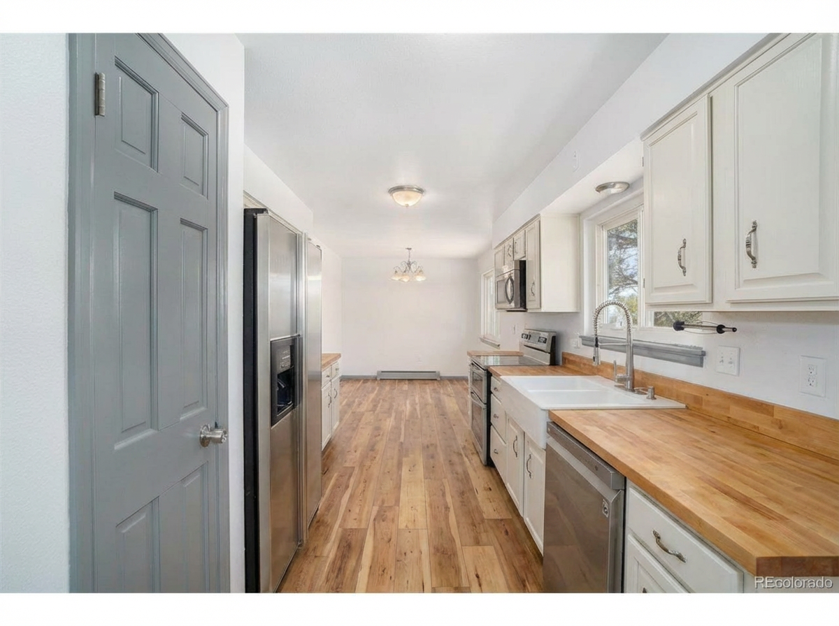 A spacious kitchen featuring stainless steel appliances, white cabinetry, and hardwood flooring with natural light through large windows