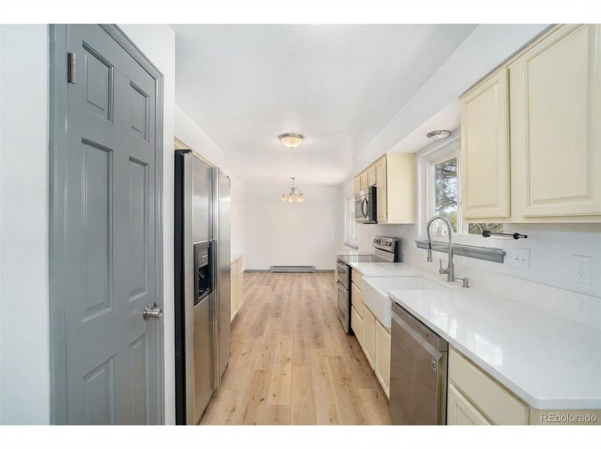Modern kitchen with stainless steel appliances, light-colored cabinets, large windows, and wooden floor