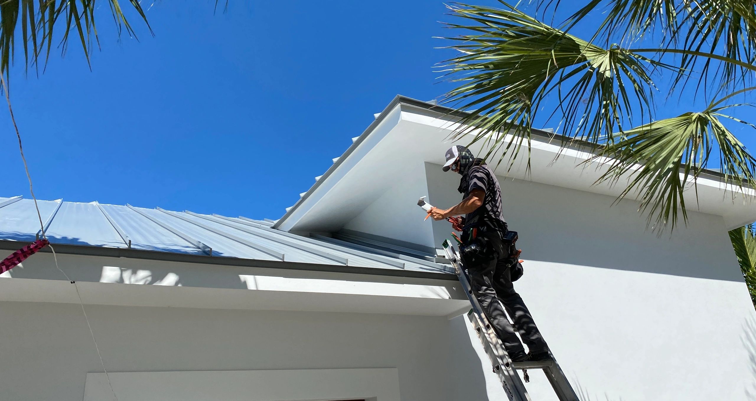 Roofer performing maintenance work on a metal roof with tropical backdrop in South Florida