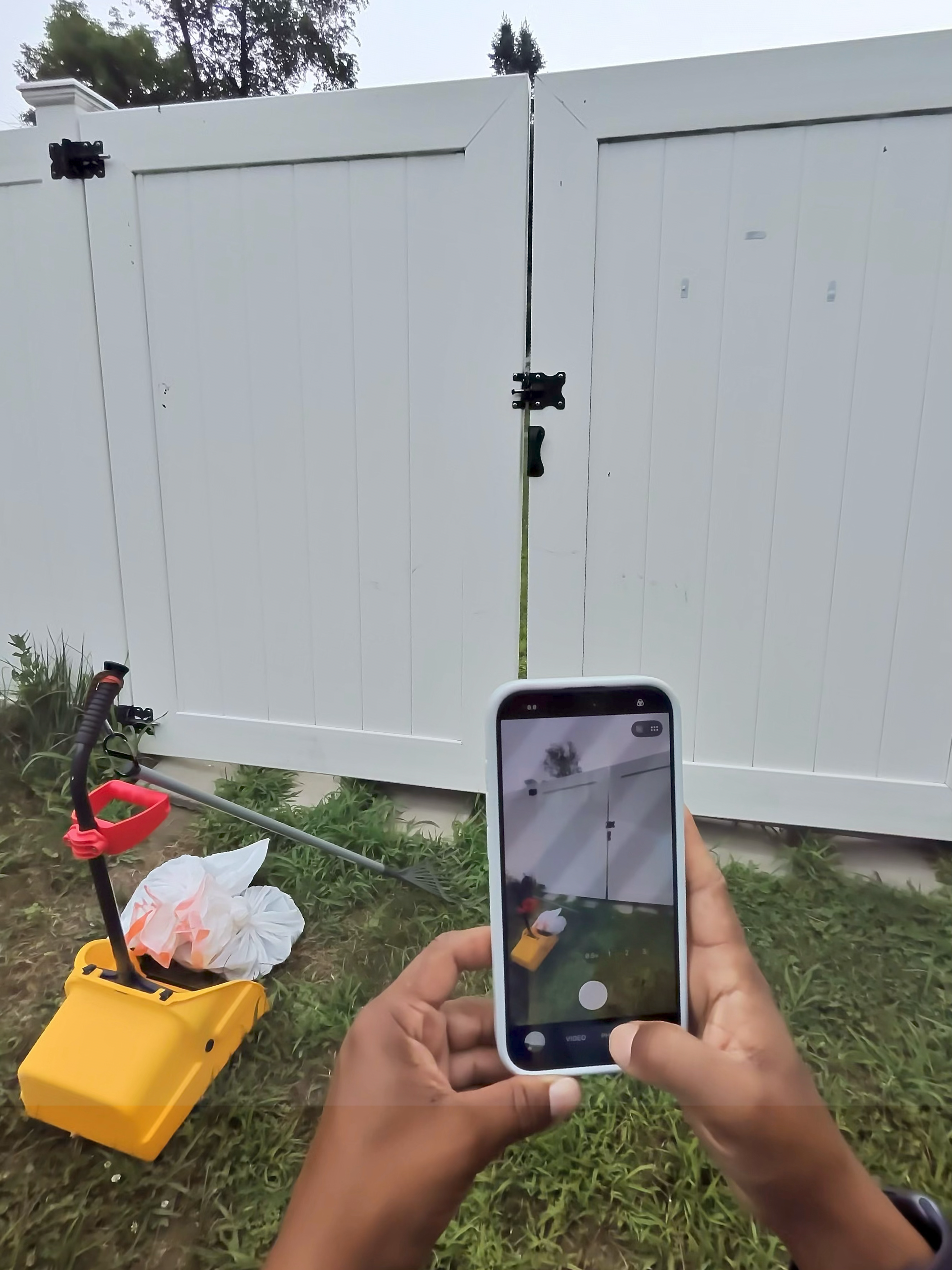 Phone taking a confirmation photo of a closed white backyard gate after a scooping visit