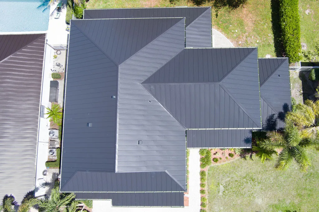 Aerial view of two modern homes featuring sleek black metal roofs with surrounding greenery and pool