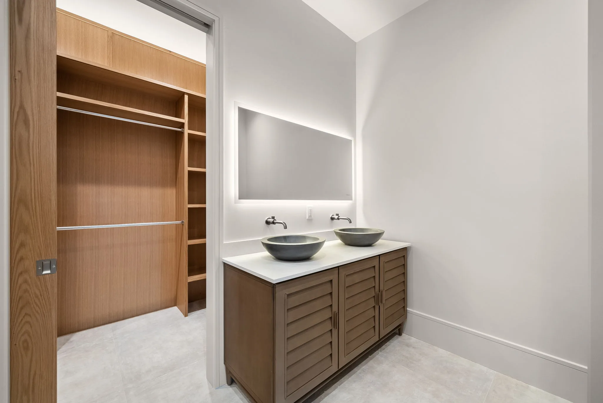 A bathroom with a double vanity, two bowl sinks and a walk-in closet alongside.