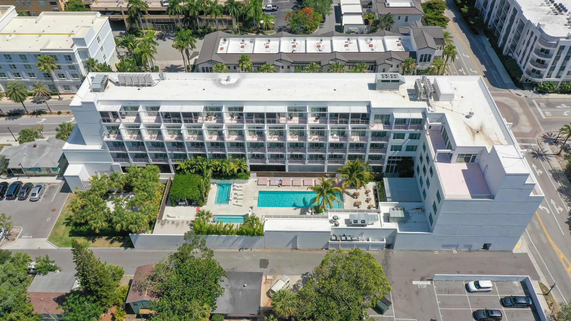 Aerial of the white multi-storey Peninsula Residences building with its pool deck, the Sarasota marina behind it.