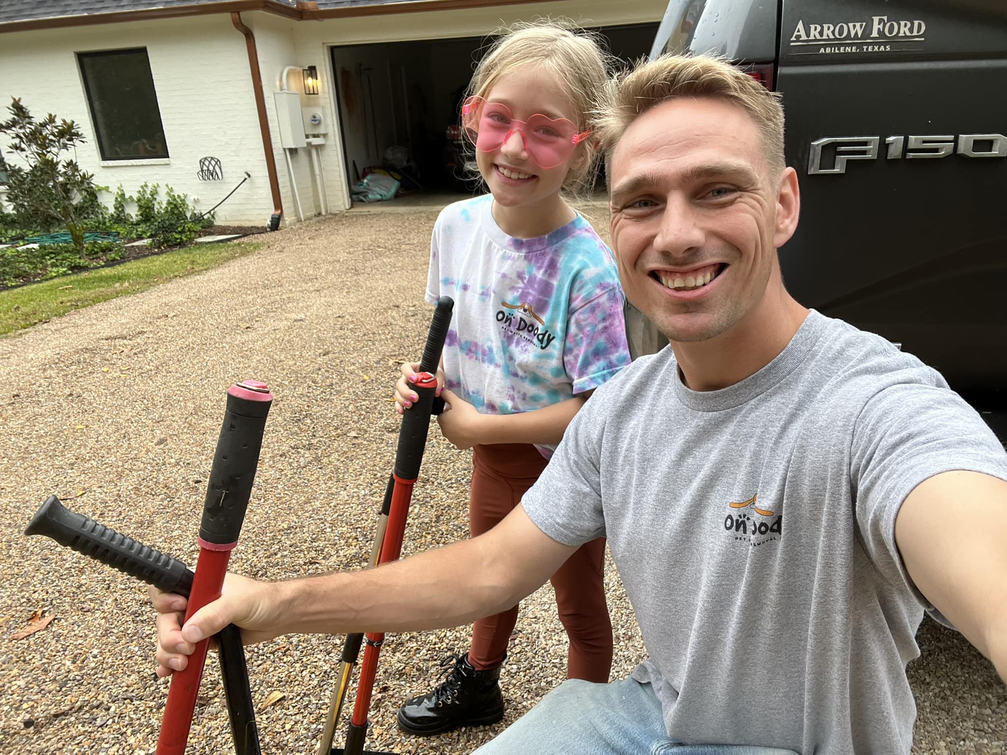Willum and his daughter posing together with colorful yard tools in their driveway