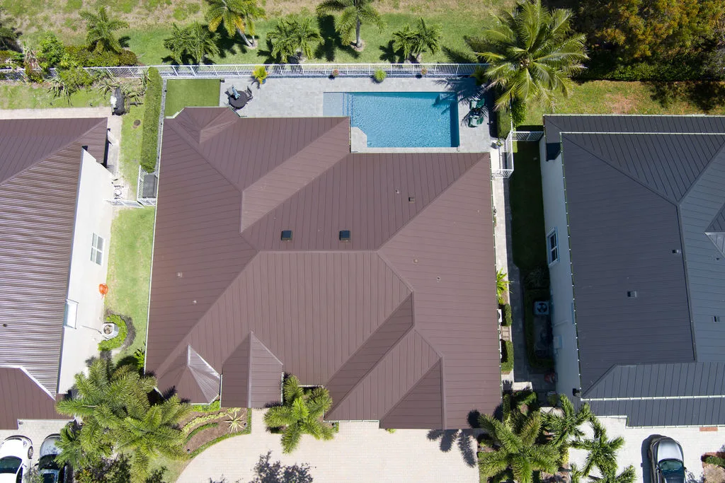 Aerial view of residential homes with brown metal roofs, pool, and palm trees on the Treasure Coast