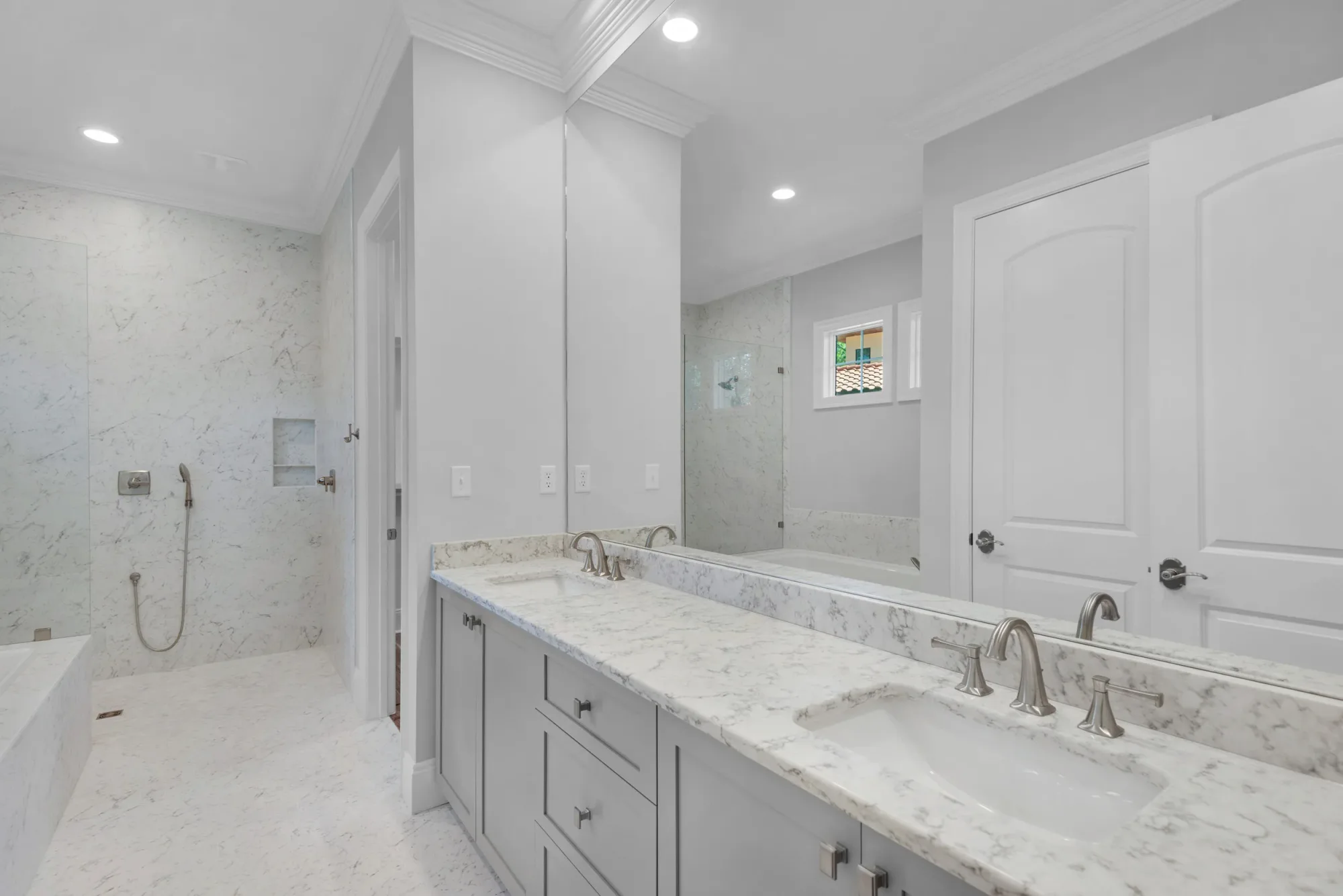 A finished primary bathroom in marble, with a curbless walk-in shower and double vanity.