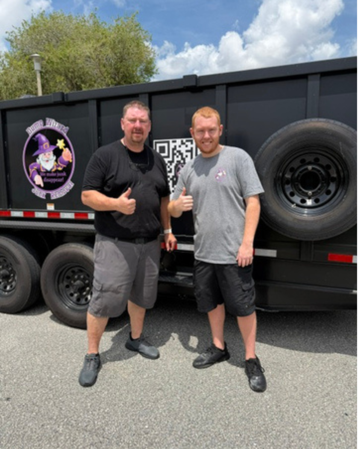 Two Dump Wizard team members giving a thumbs up beside the wrapped black trailer