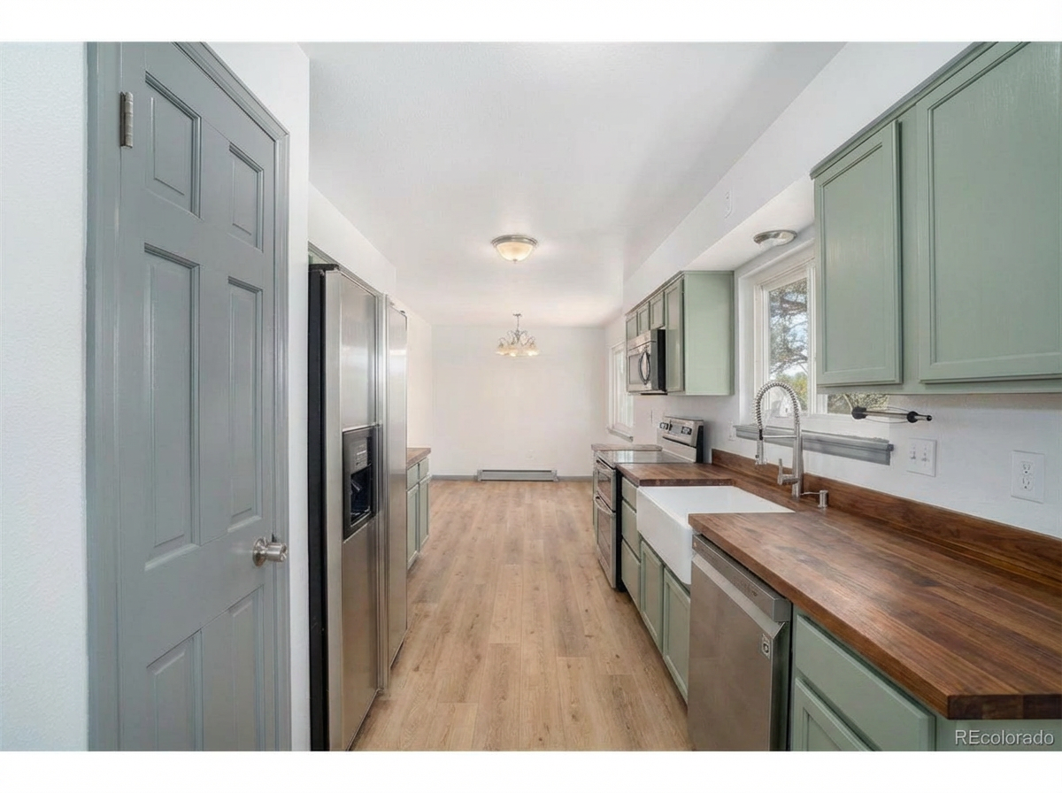 Spacious kitchen with light green cabinets, wooden countertops, and stainless steel appliances