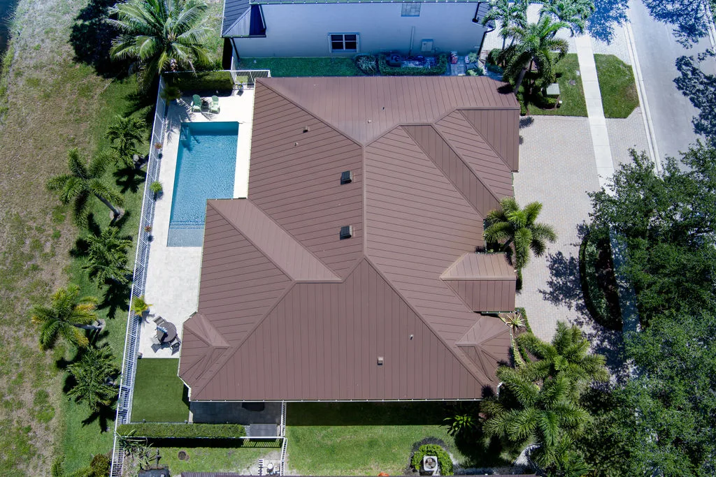 Aerial view of a modern single-story home with a brown metal roof, pool, and landscaped yard