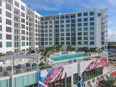 A contemporary apartment building featuring large windows, a swimming pool, and landscaped outdoor areas. The structure showcases a vibrant mural on the lower level and includes multiple levels of residential units.