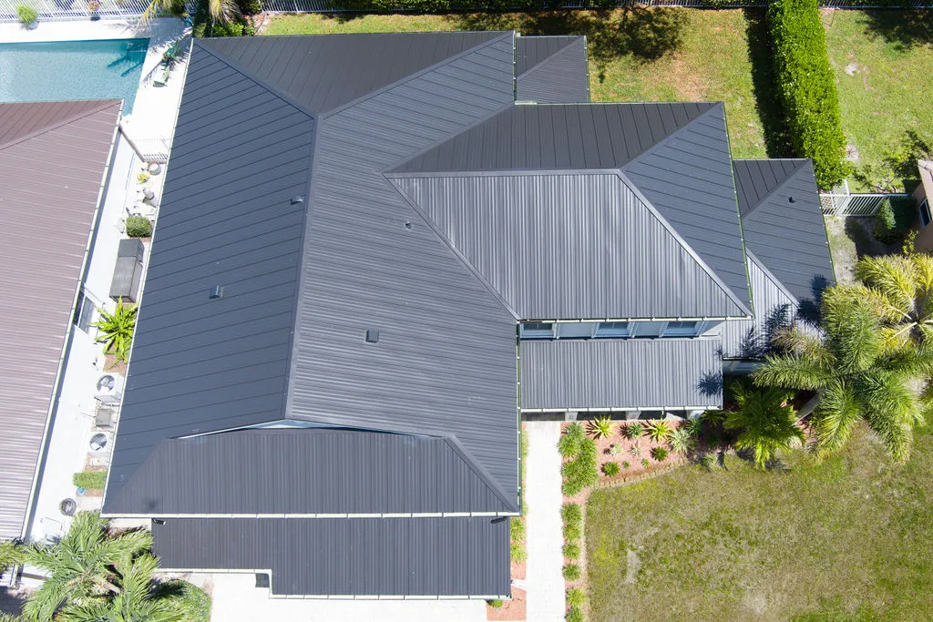 Aerial view of a modern home with a dark metal roof, pool, and lush greenery on the Treasure Coast
