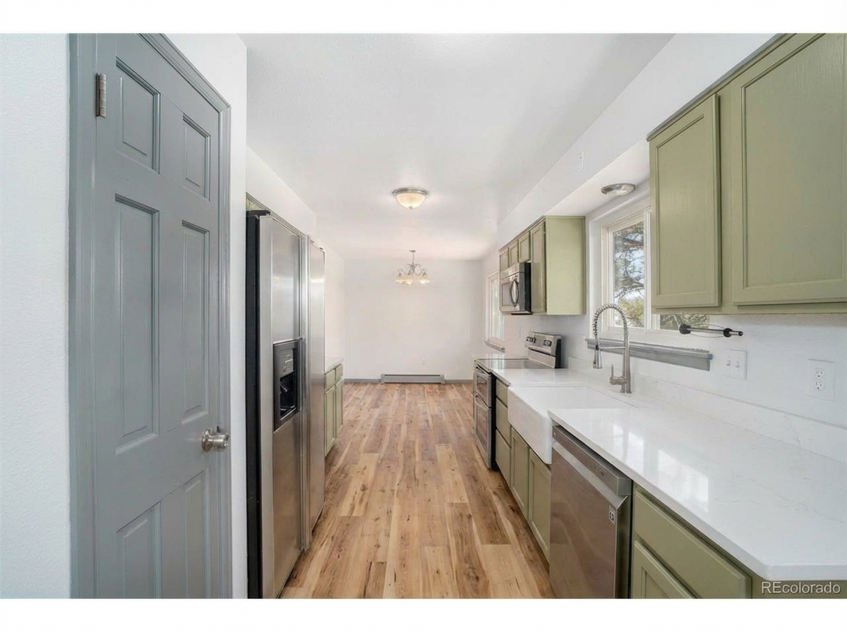 Spacious modern kitchen featuring light green cabinetry, stainless steel appliances, and hardwood flooring