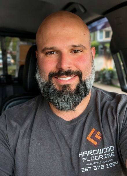 Christopher Gross smiling in his vehicle, wearing his Hardwood Flooring by Christopher shirt