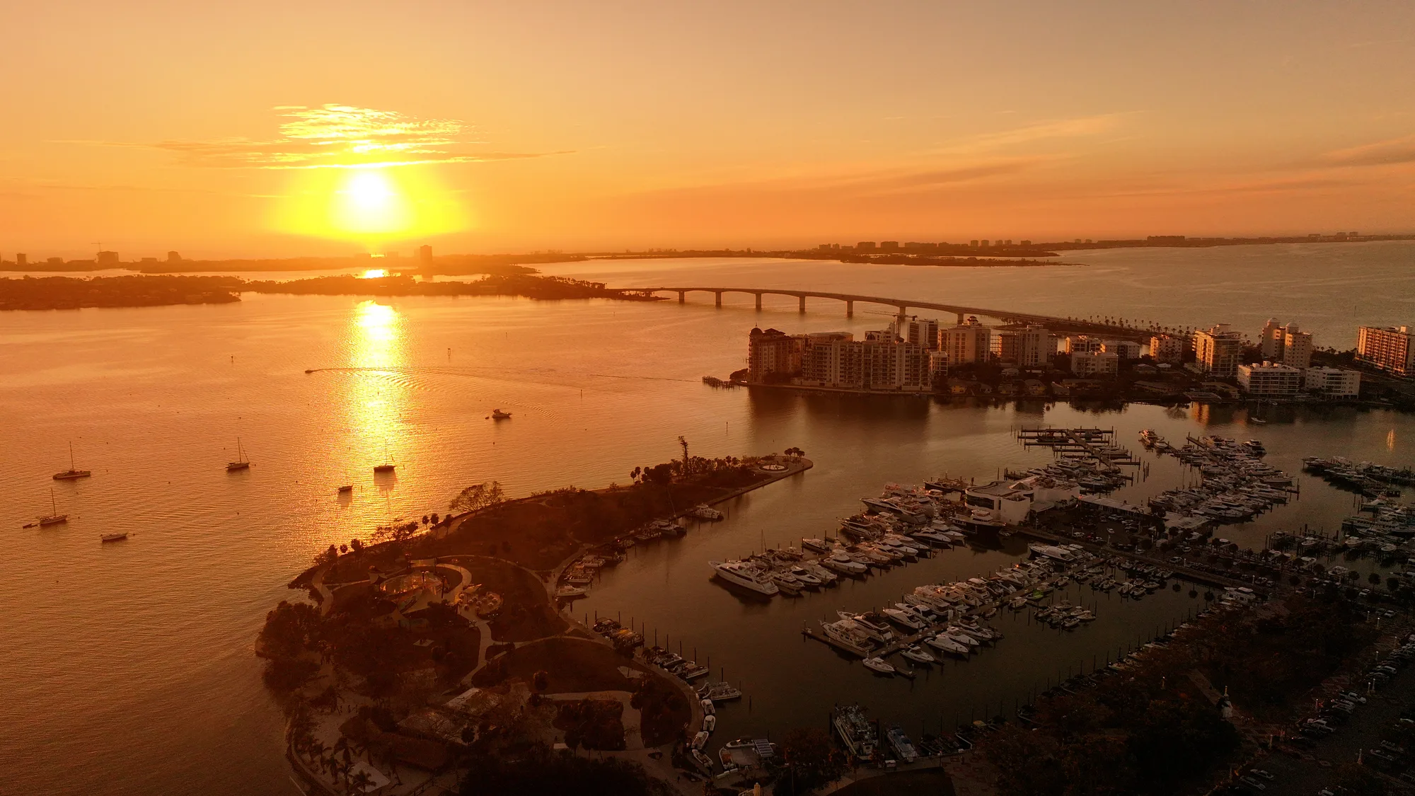 Aerial photograph at sunset looking across downtown Sarasota's waterfront towers to the Ringling Bridge and the Gulf beyond.