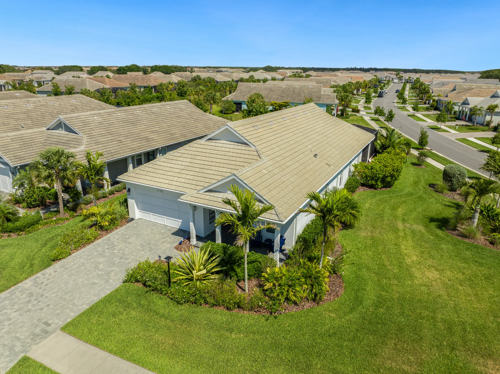 This image features a single-story suburban home with a landscaped yard and stone driveway, surrounded by similar residences. The clear blue sky enhances the peaceful neighborhood atmosphere.