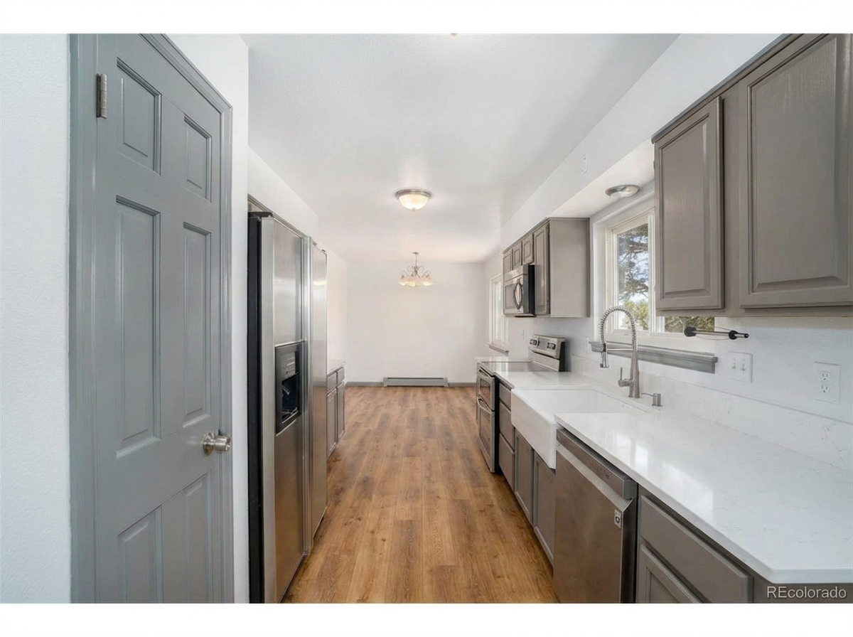 Contemporary kitchen with gray cabinetry, stainless steel appliances, sleek white countertops, and wooden flooring