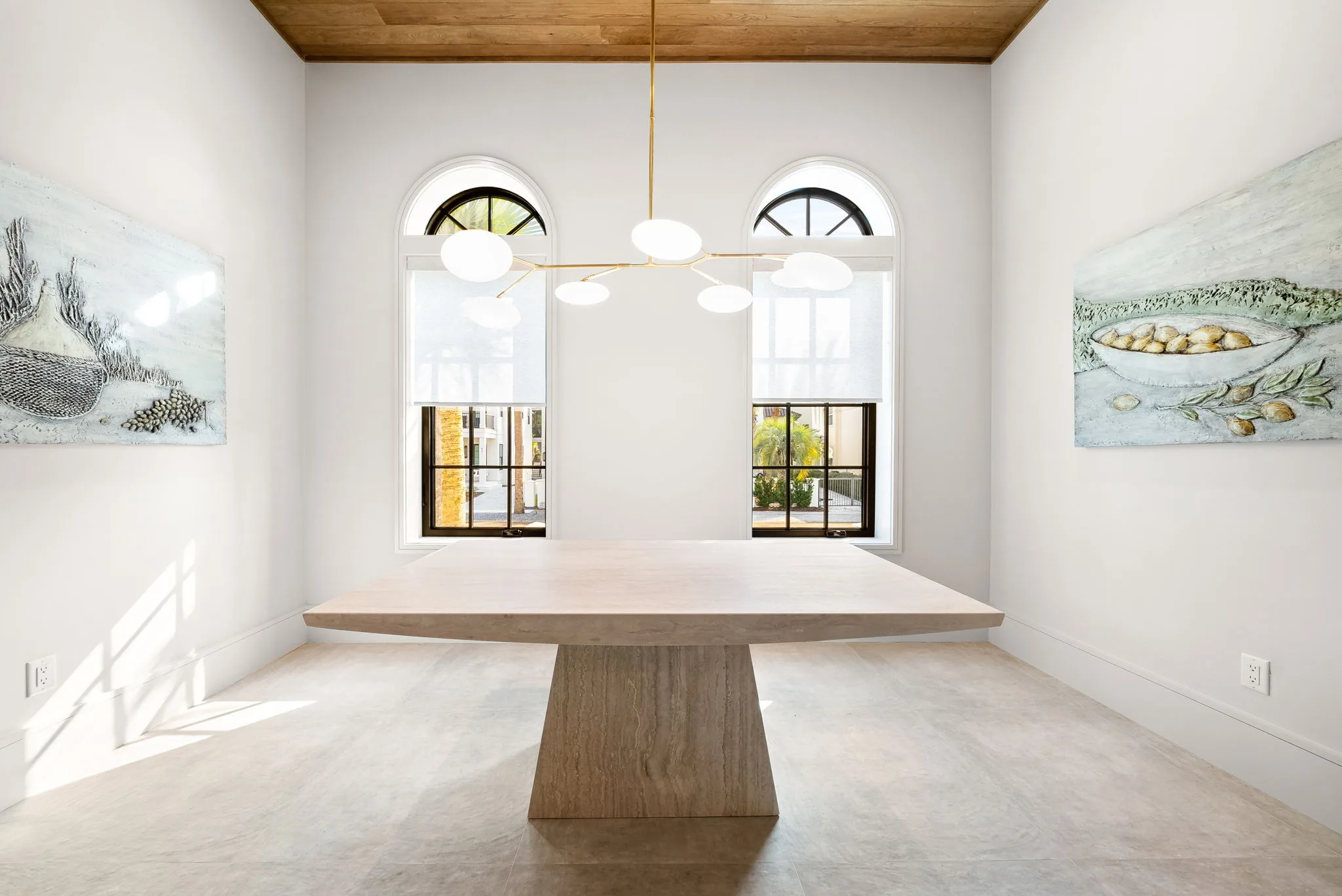 A dining room with a large wooden table, modern chandelier and arched windows.