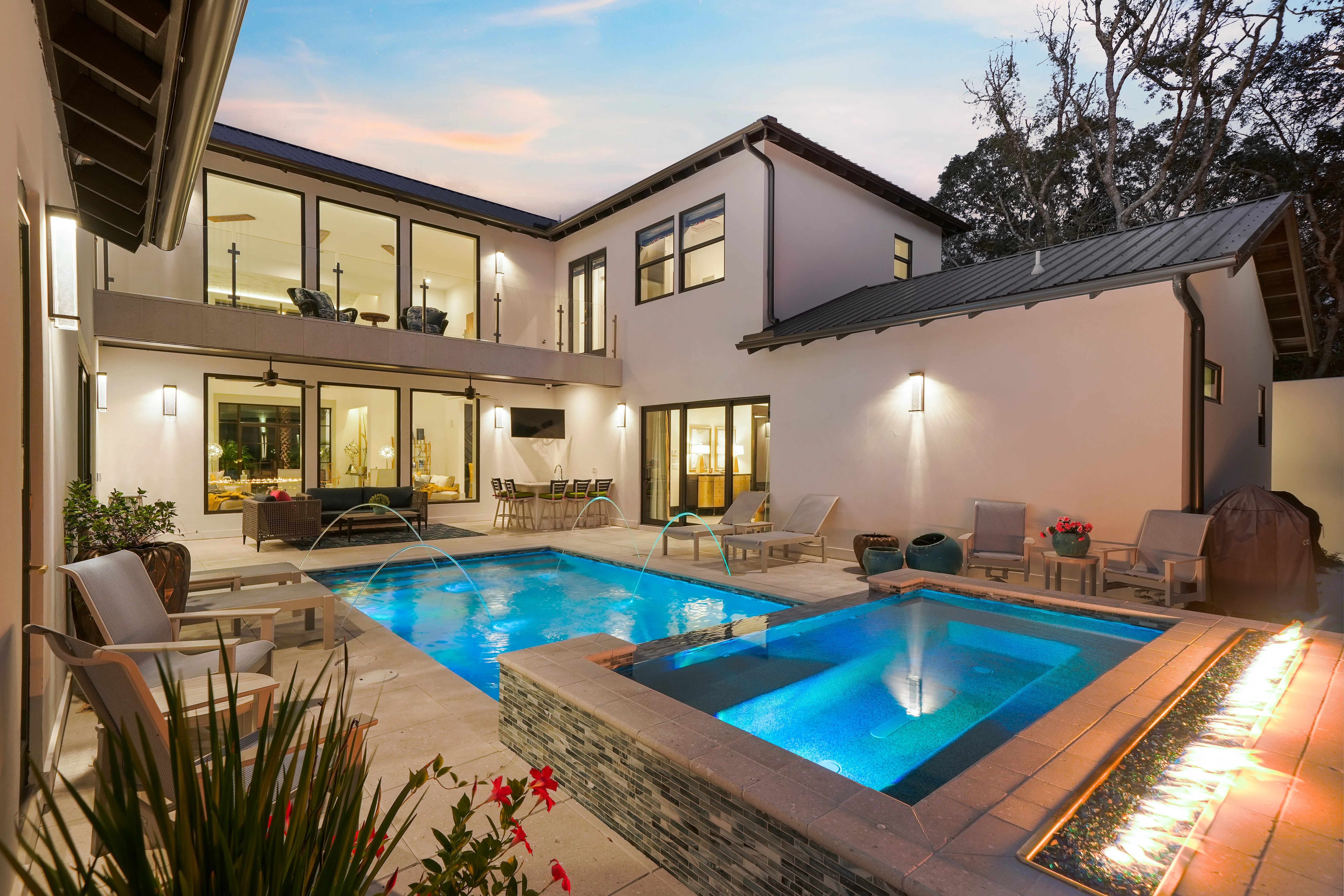 A swimming pool at dusk with a lit modern house behind it.