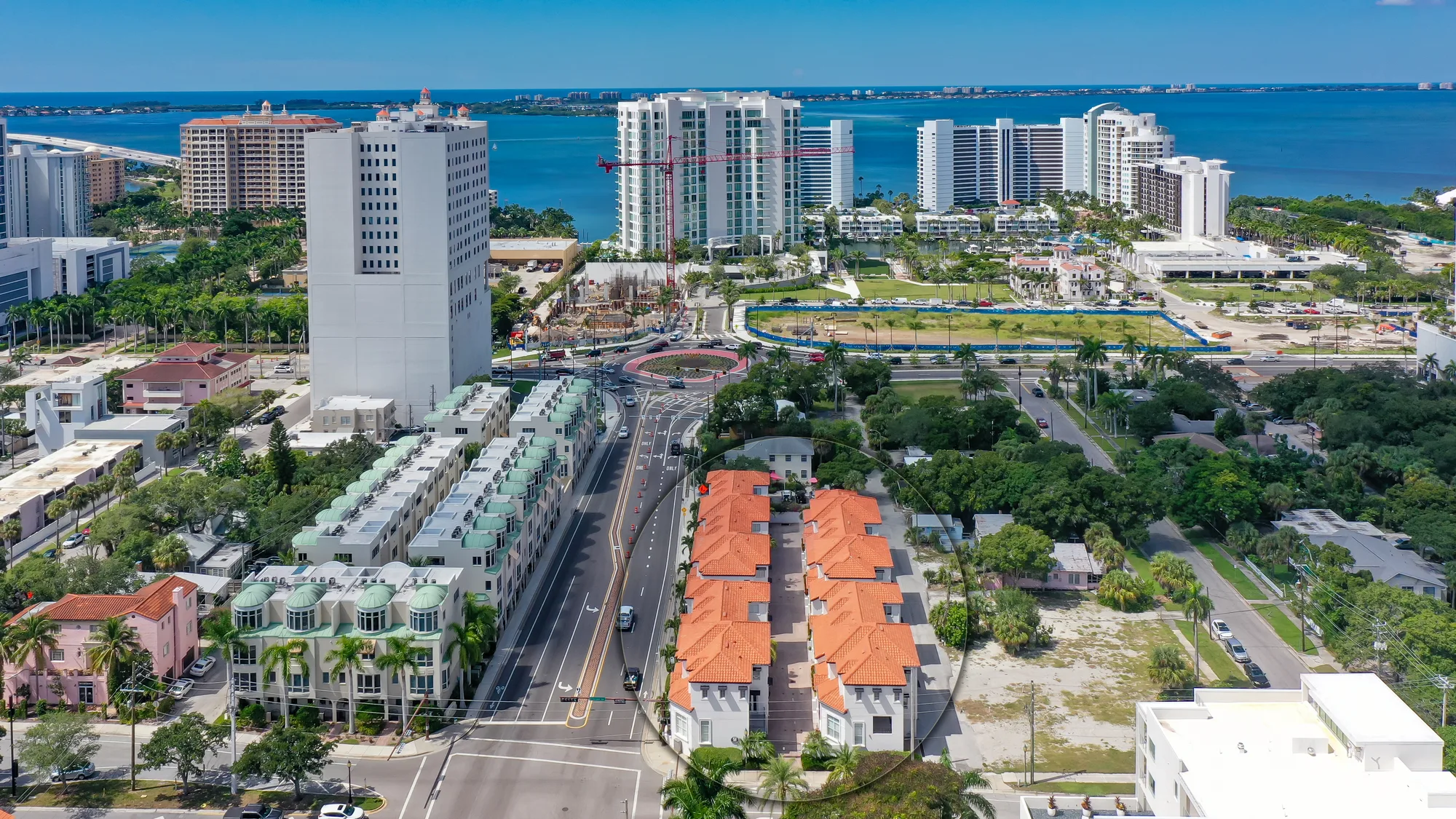 An aerial view of a coastal urban area showcasing a mix of high-rise buildings, residential complexes, and green spaces along the waterfront. The image captures ongoing construction activities and roadways, highlighting the development and infrastructure in the region.