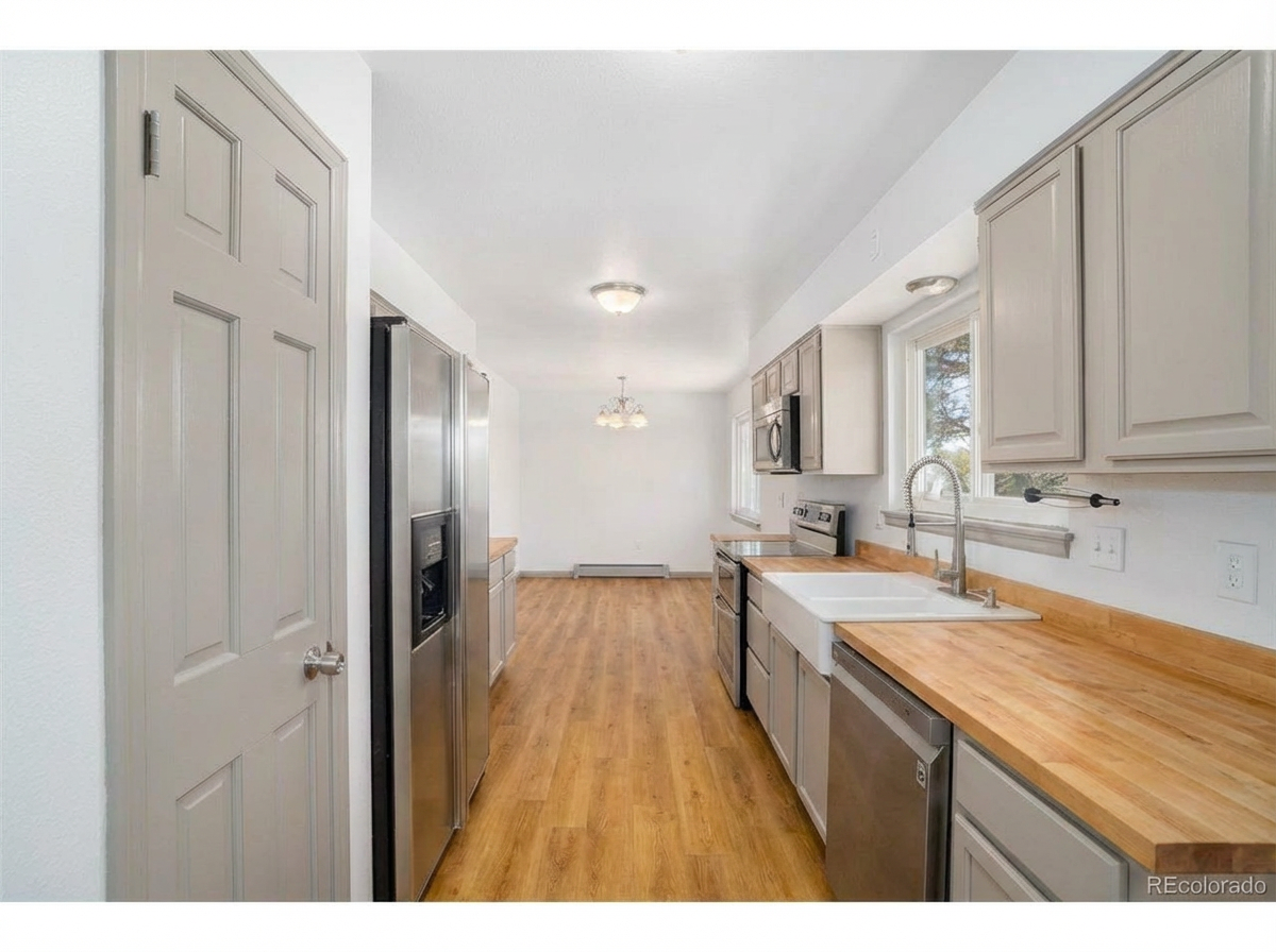Modern kitchen with stainless steel appliances, light cabinetry, and wooden countertops with natural light