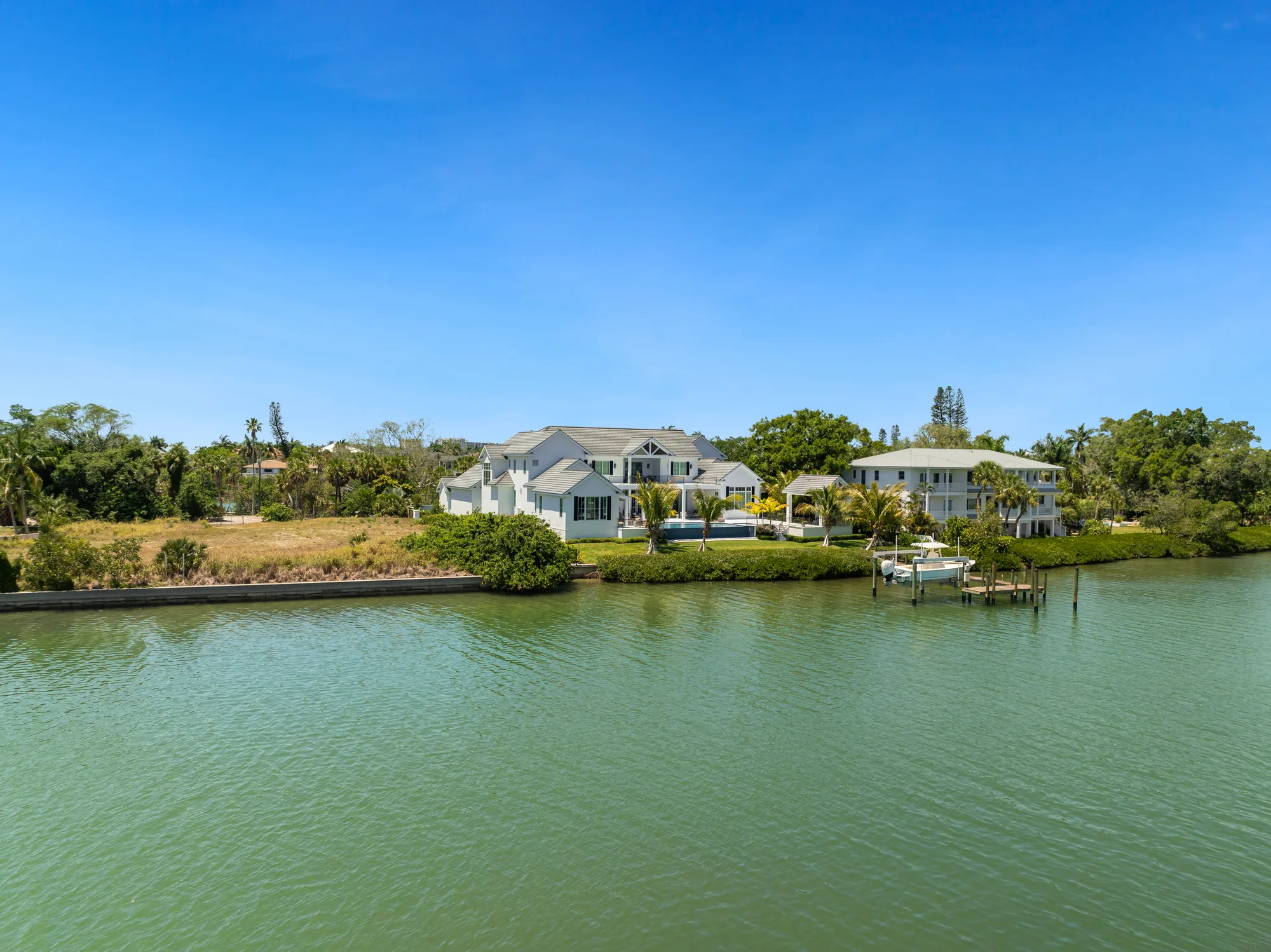 Aerial view from the water of a two-storey custom waterfront home with a tile roof and mature palms, on a Sarasota bayfront lot.