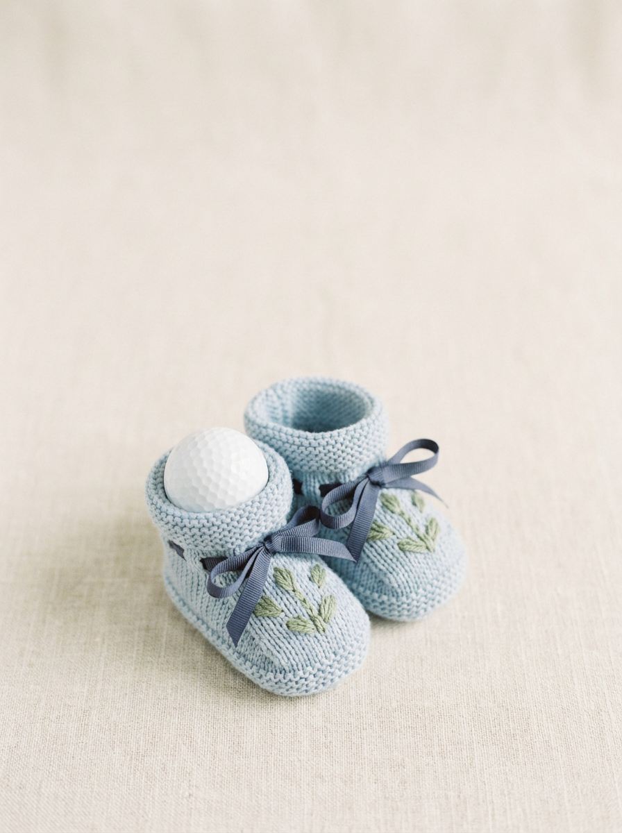Knitted baby booties with golf ball showing blue booties with green embroidery and navy ribbons