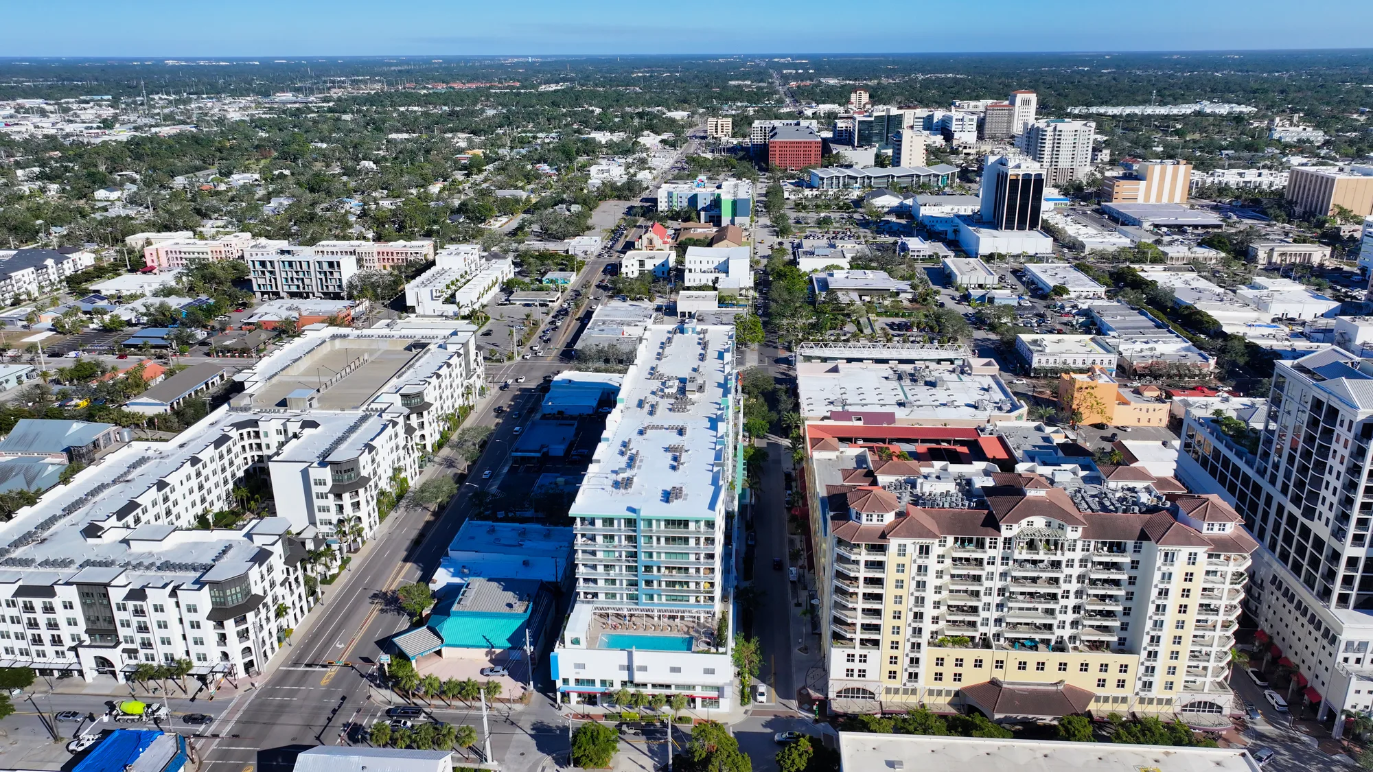 Aerial perspective of a bustling urban area featuring a mix of modern residential buildings and commercial spaces. The scene includes greenery in the background, highlighting the blend of city life and nature.
