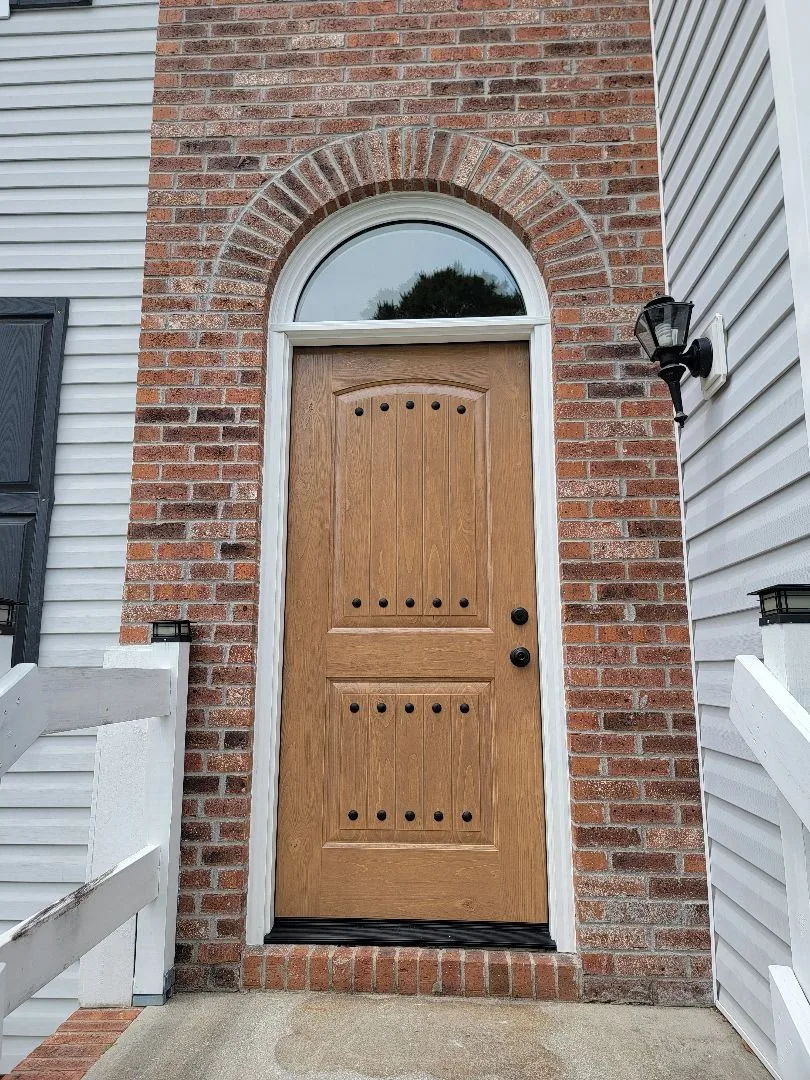 Wooden front door with arched window and vertical panels in a brick archway