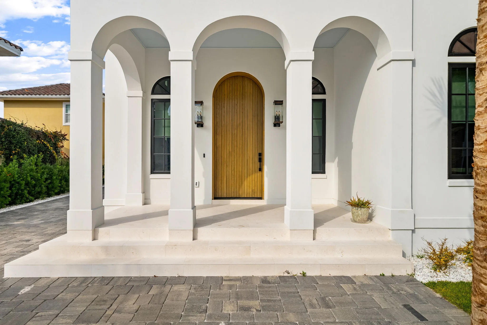 The entrance of a finished home with a tall wooden door framed by white arches and columns.