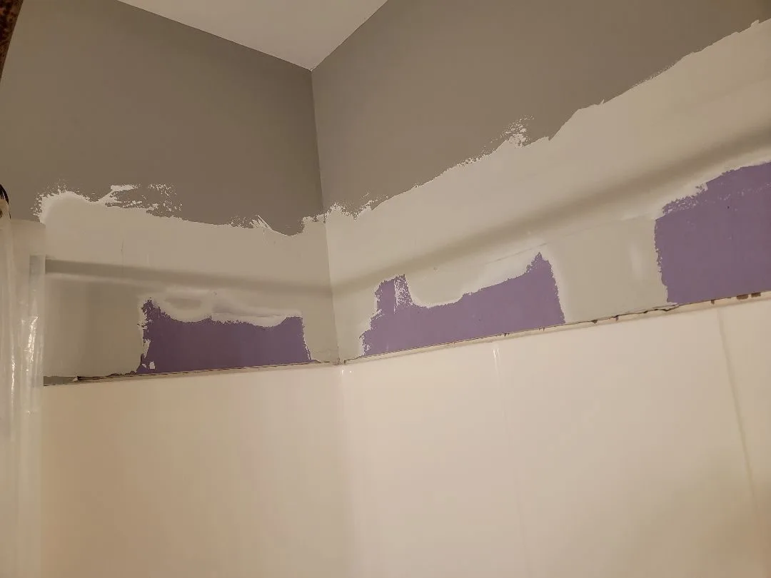 Bathroom wall mid-paint with fresh gray coat being applied over existing surface