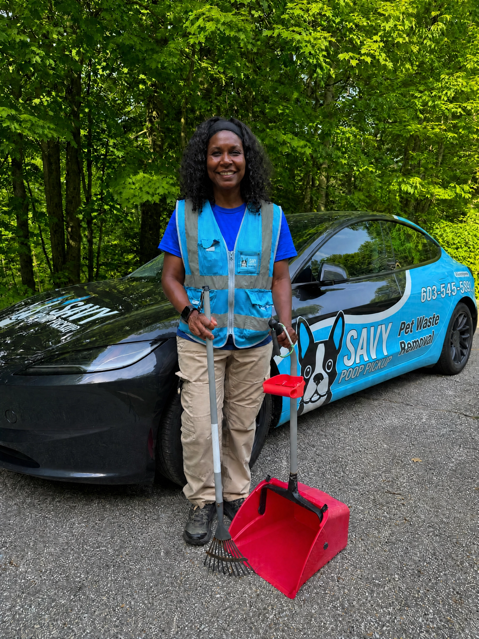 Silvia holding a rake and a red pooper scooper in front of the Savy Poop Pickup vehicle