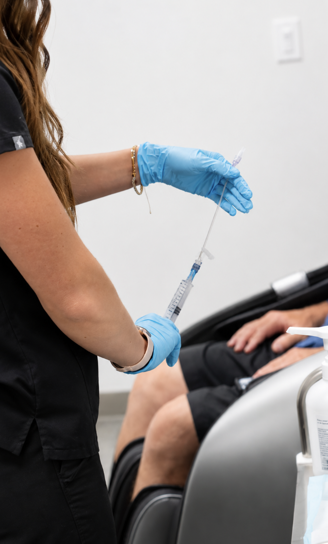 A healthcare professional wearing blue gloves holding a syringe, preparing to administer an injection in a clinical setting.