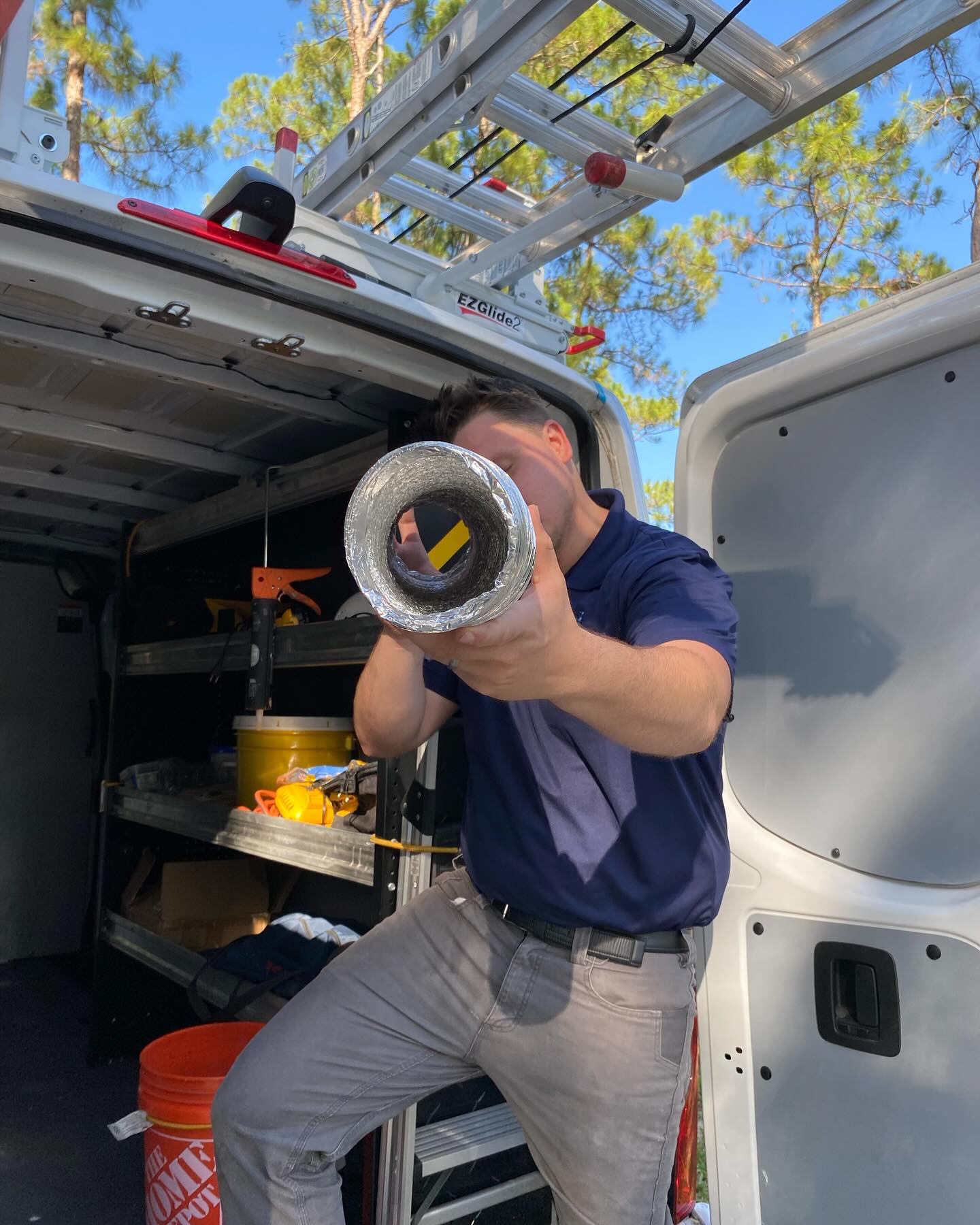 A worker holding a section of ducting material in the doorway of a service van