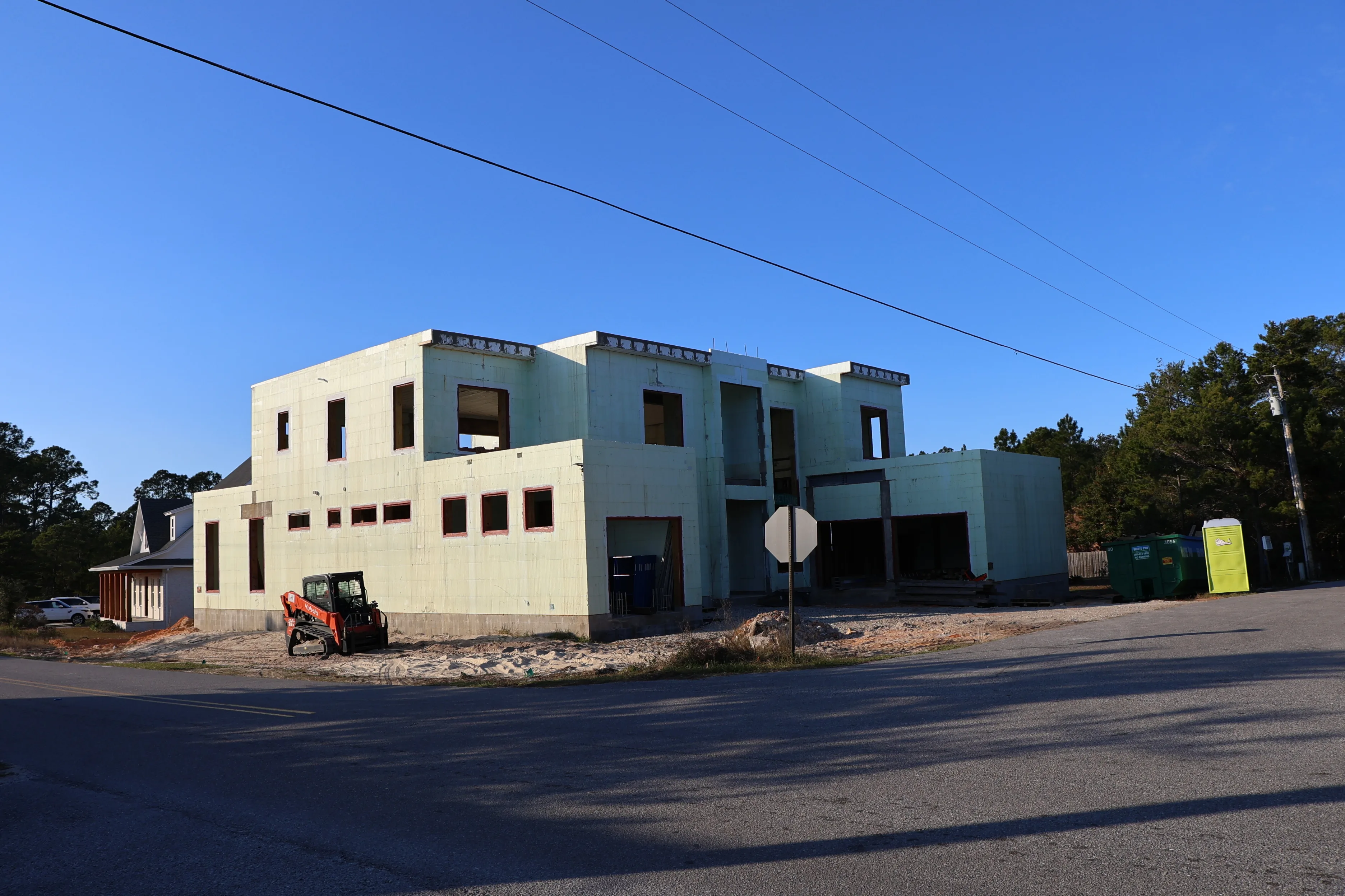 A large ICF house shell under construction seen from the road, with a dumpster and equipment on site.