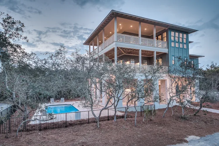 A three-storey coastal home among pine trees with a swimming pool below.