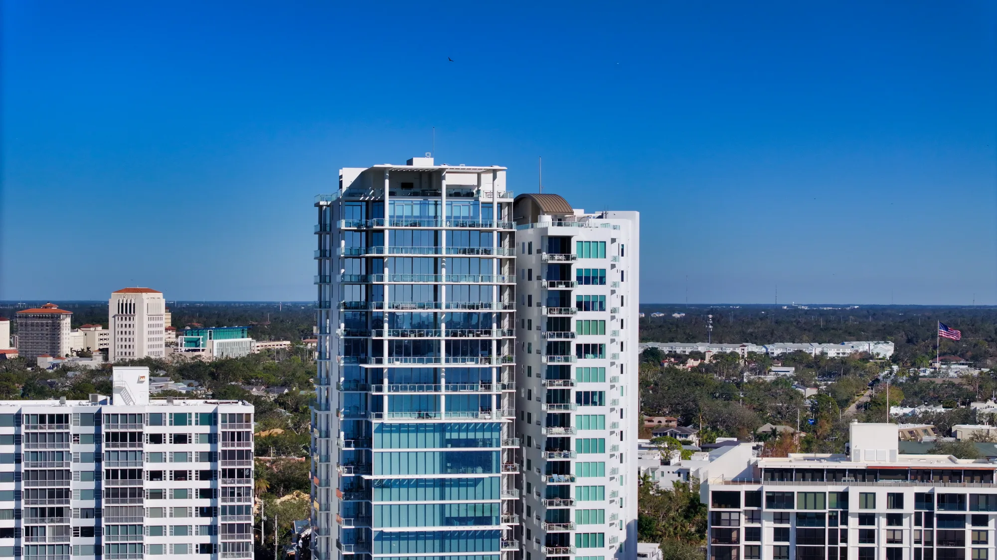 The Epoch tower seen from the air with the low-rise Sarasota skyline and treeline behind.